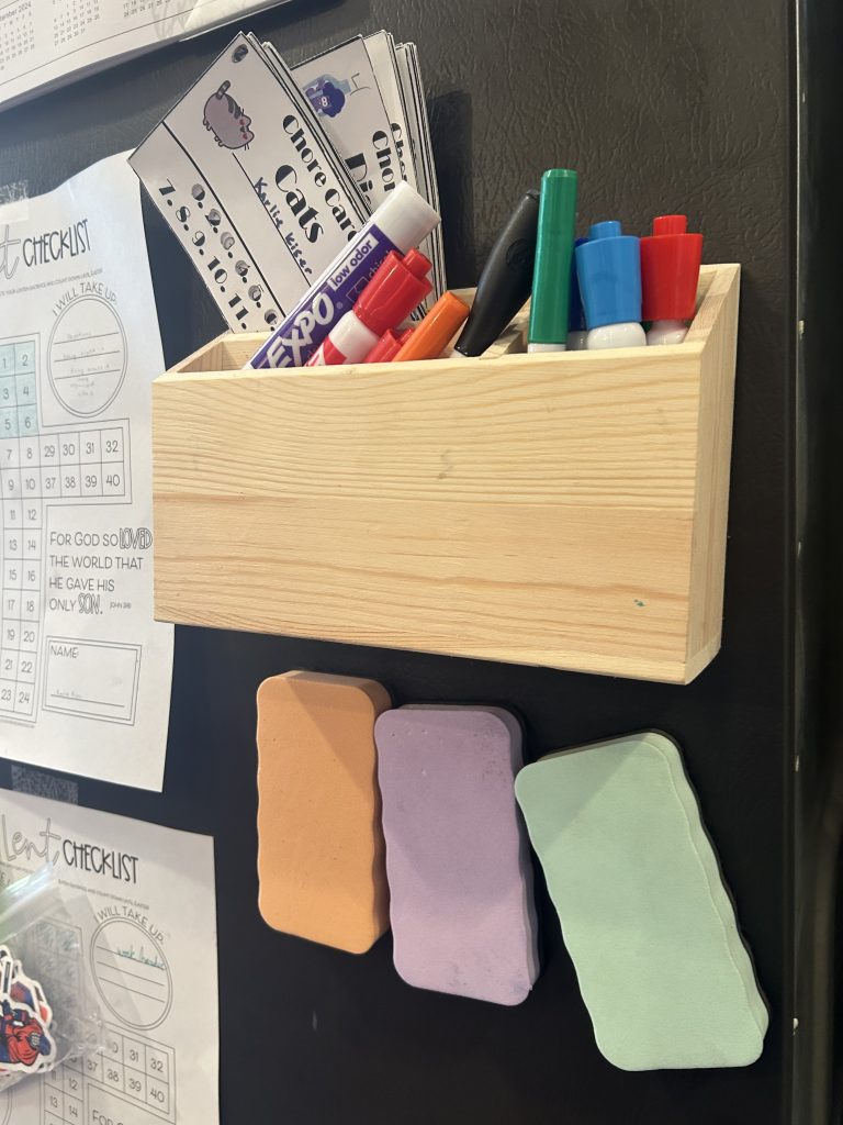 dry erase markers in a box with dry erase erasers on a refrigerator