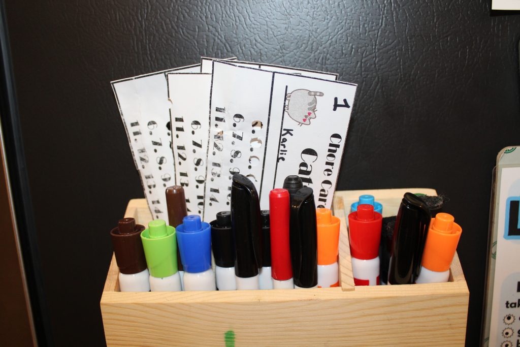 Chore cards stored in a magnetic box on the fridge with dry erase markers
